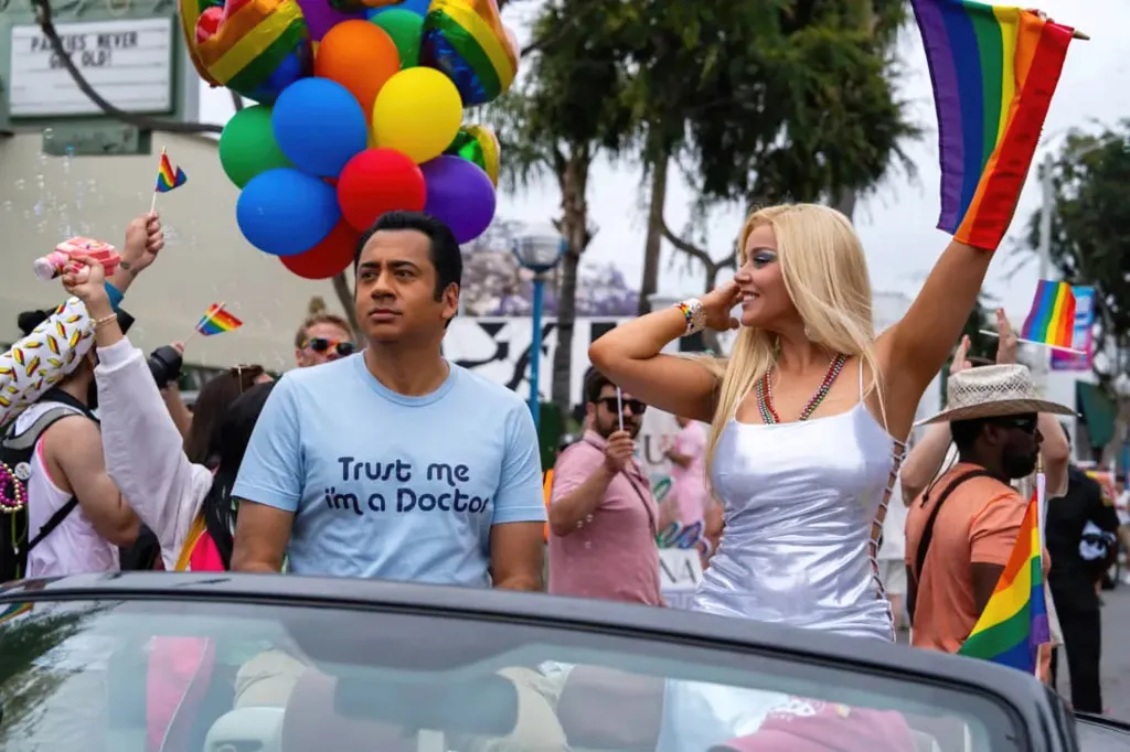 Kal Penn, in a blue T-shirt, as Dr. Sandeep Kapoor and Abbie Cornish, in a white tank top, as Anna Nicole Smith ride in a convertible during a parade.