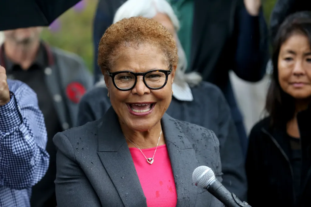 Karen Bass speaking into a microphone while surrounded by supporters and media.
