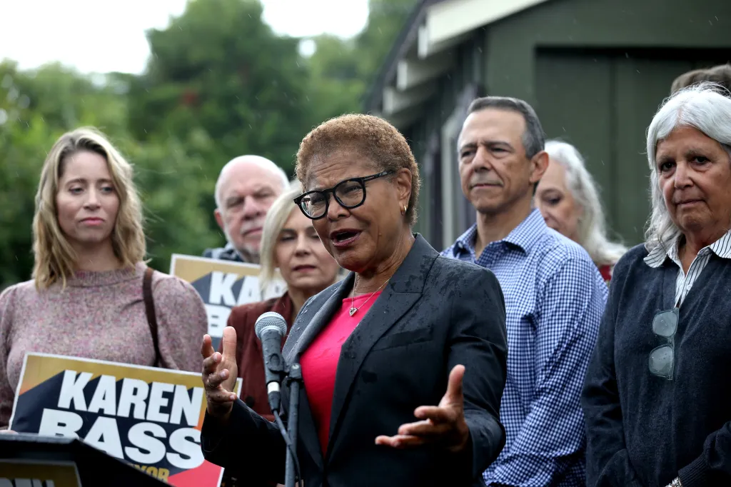 Karen Bass speaks to the media during a campaign stop, surrounded by supporters and campaign signs.