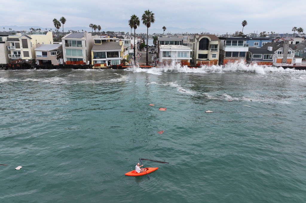 A kayaker watches waves hit a walkway in front of homes in Long Beach, Calif., as Tropical Storm Rachel approaches.