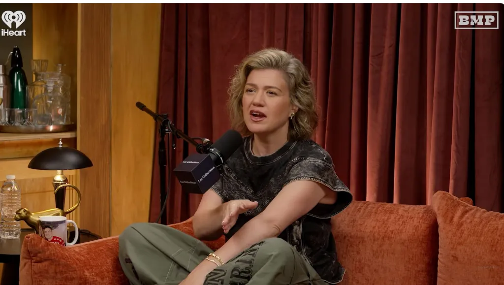Kelly Clarkson sitting on a couch and speaking into a microphone.