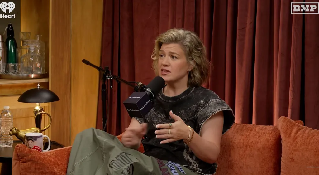Kelly Clarkson speaking into a microphone while sitting on a couch.