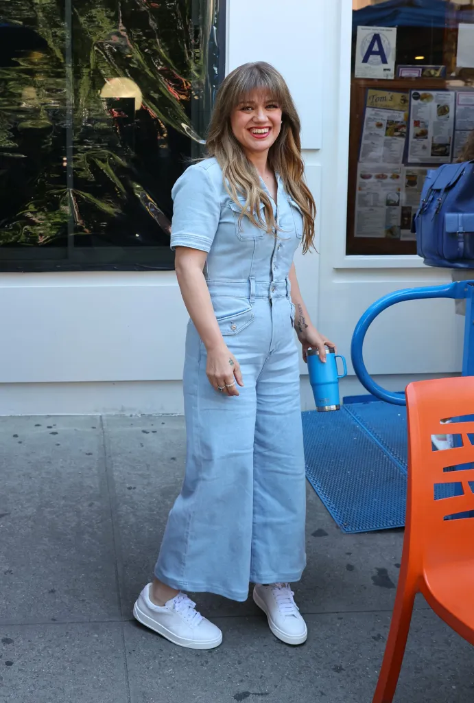 Kelly Clarkson wearing a light blue denim jumpsuit and white sneakers outside Tom's Restaurant in New York City.