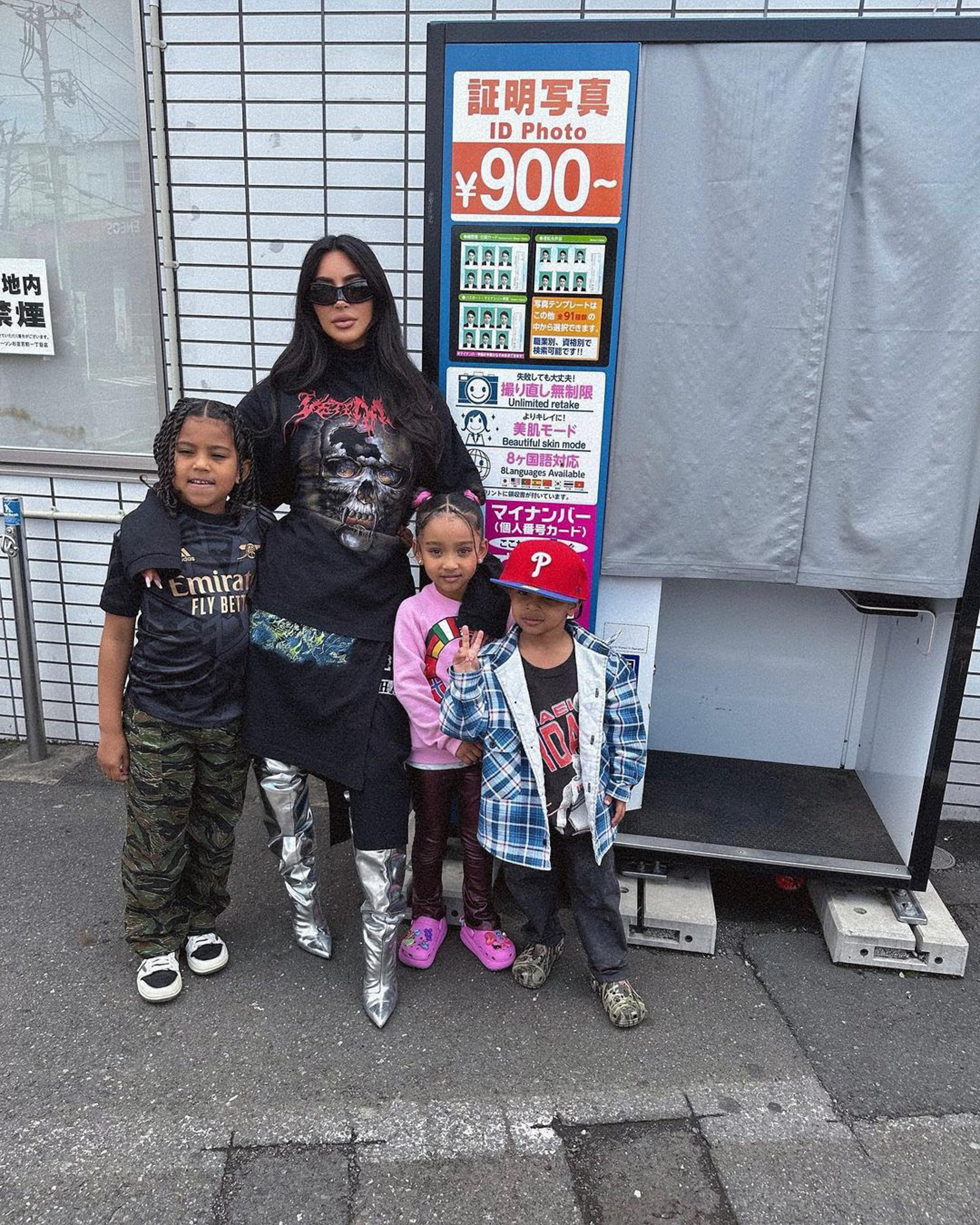Kim Kardashian standing with her children in front of a Japanese photo booth.