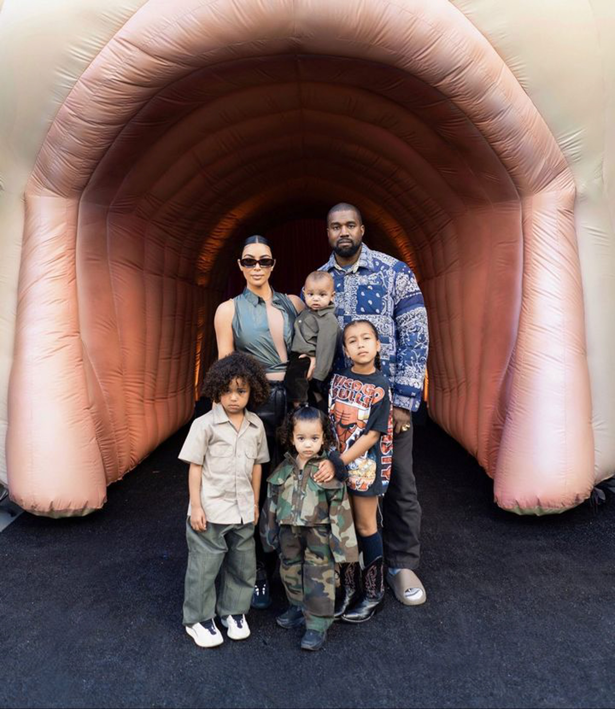 Kim Kardashian and Kanye West pose with their children North, Chicago, Psalm, and Saint West in front of a large, flesh-toned inflatable structure.