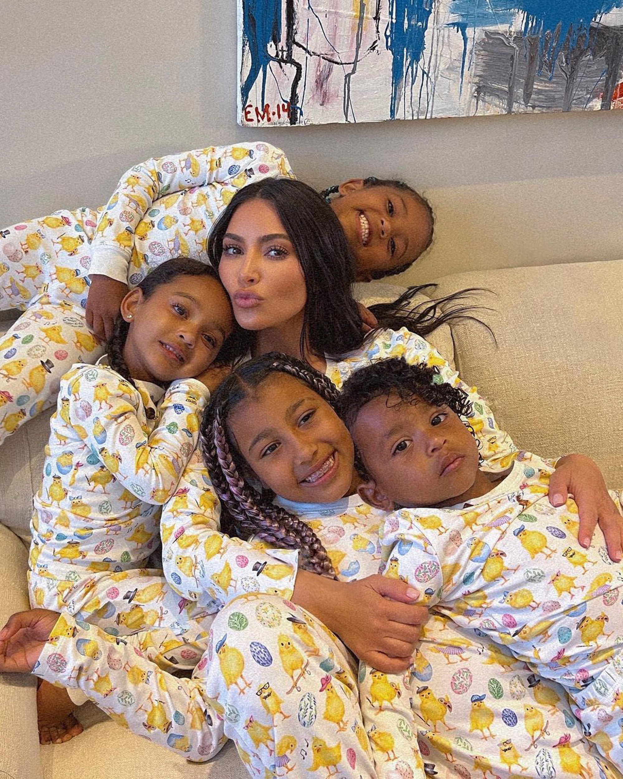 Kim Kardashian and her five children—North, Saint, Chicago, Psalm, and Chicago—lying together on a couch, all wearing matching Easter-themed pajamas.