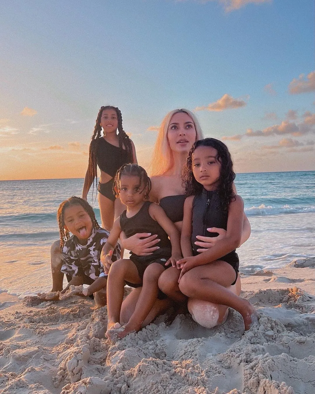 Kim Kardashian poses on a sandy beach at sunset with her four children, North, Saint, Chicago, and Psalm.