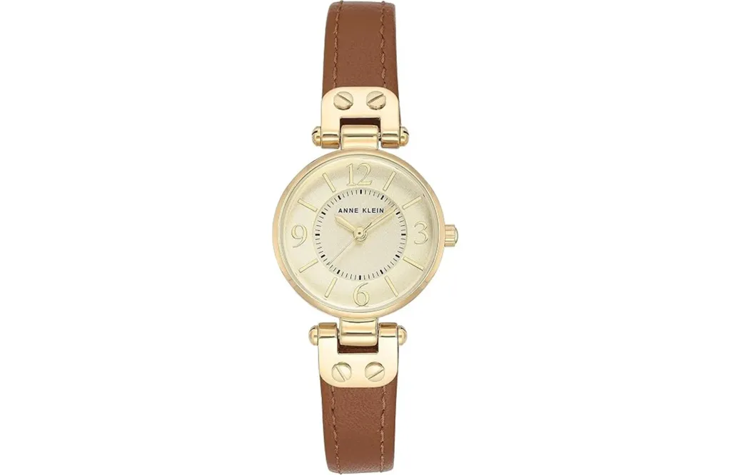 Anne Klein women's watch with a gold-colored case, a cream-colored dial with gold markings, and a brown leather strap.