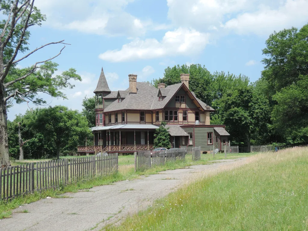 The Kreischer Mansion, a historic 2.5-story Victorian residence, stands behind a wooden fence along a paved road.