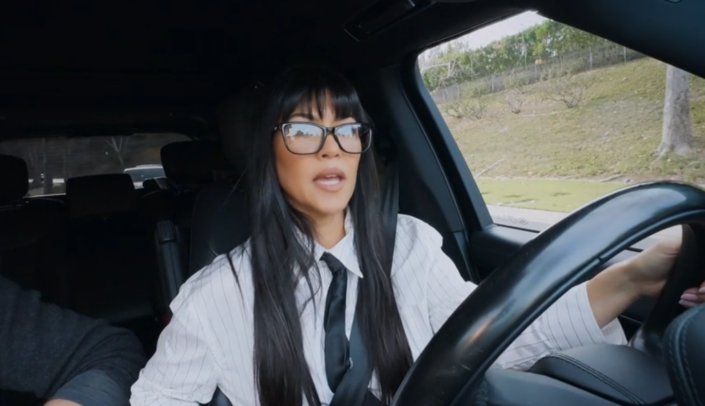 Kourtney Kardashian driving a car while wearing glasses.