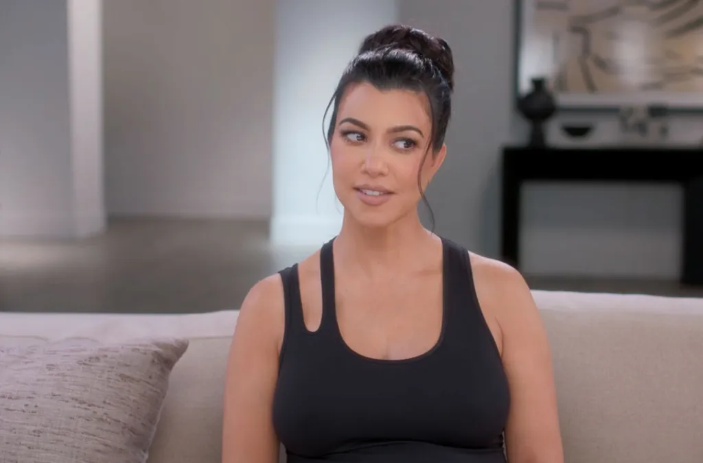 Kourtney Kardashian sitting on a couch, wearing a black tank top, with her hair in a bun.