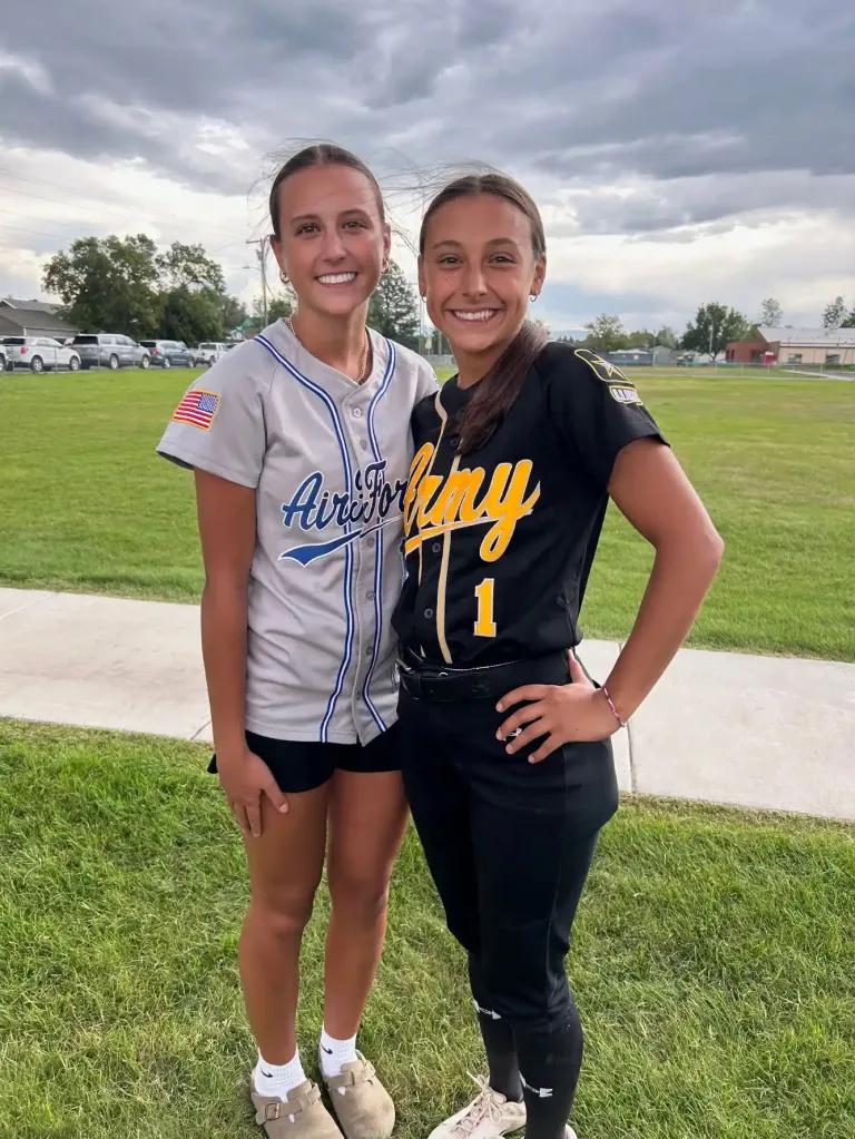 Kyann Dean and Samantha Rensvold stand outdoors in sports uniforms, with Dean on the left in a grey Air Force jersey and Rensvold on the right in a black Army uniform.