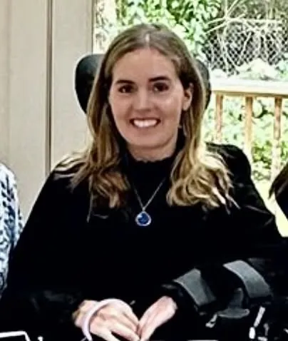 Kyle Kennedy smiling while wearing a black top and a pendant necklace.