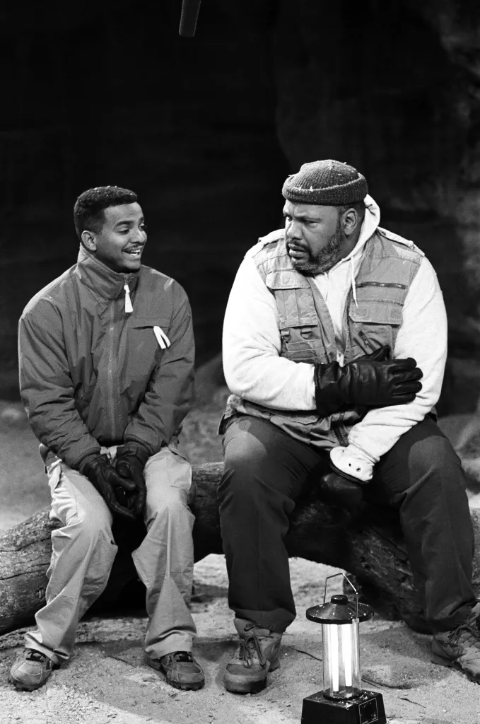 Black-and-white photo of Alfonso Ribeiro as Carlton Banks and James Avery as Philip Banks sitting on a log with a lantern in 
