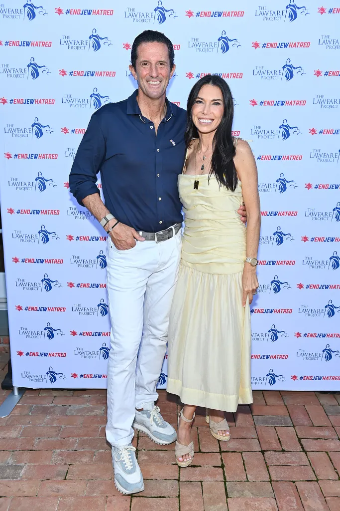 Anthony Westreich and Tanya Zuckerbrot pose together in front of a branded backdrop at a garden reception.