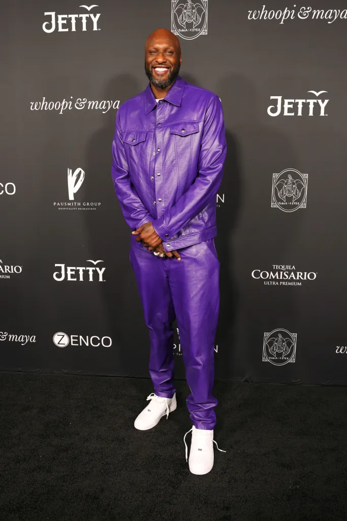 Lamar Odom wearing a matching purple jacket and pants in front of a branded step-and-repeat backdrop.