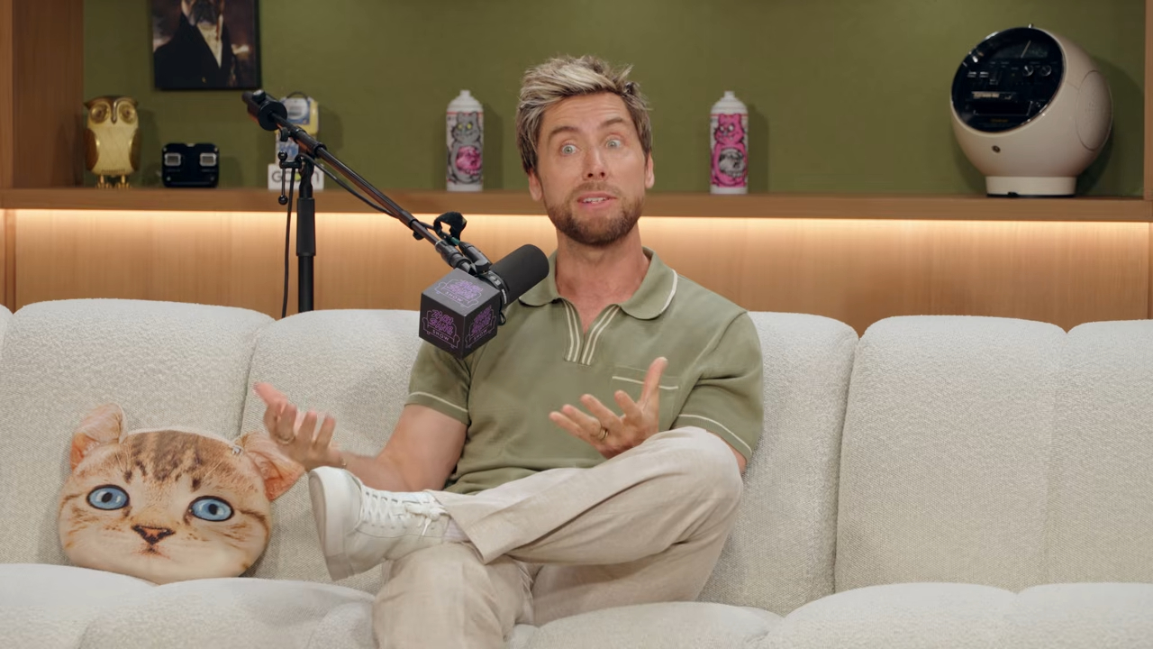 Lance Bass sitting on a couch on a talk show set.