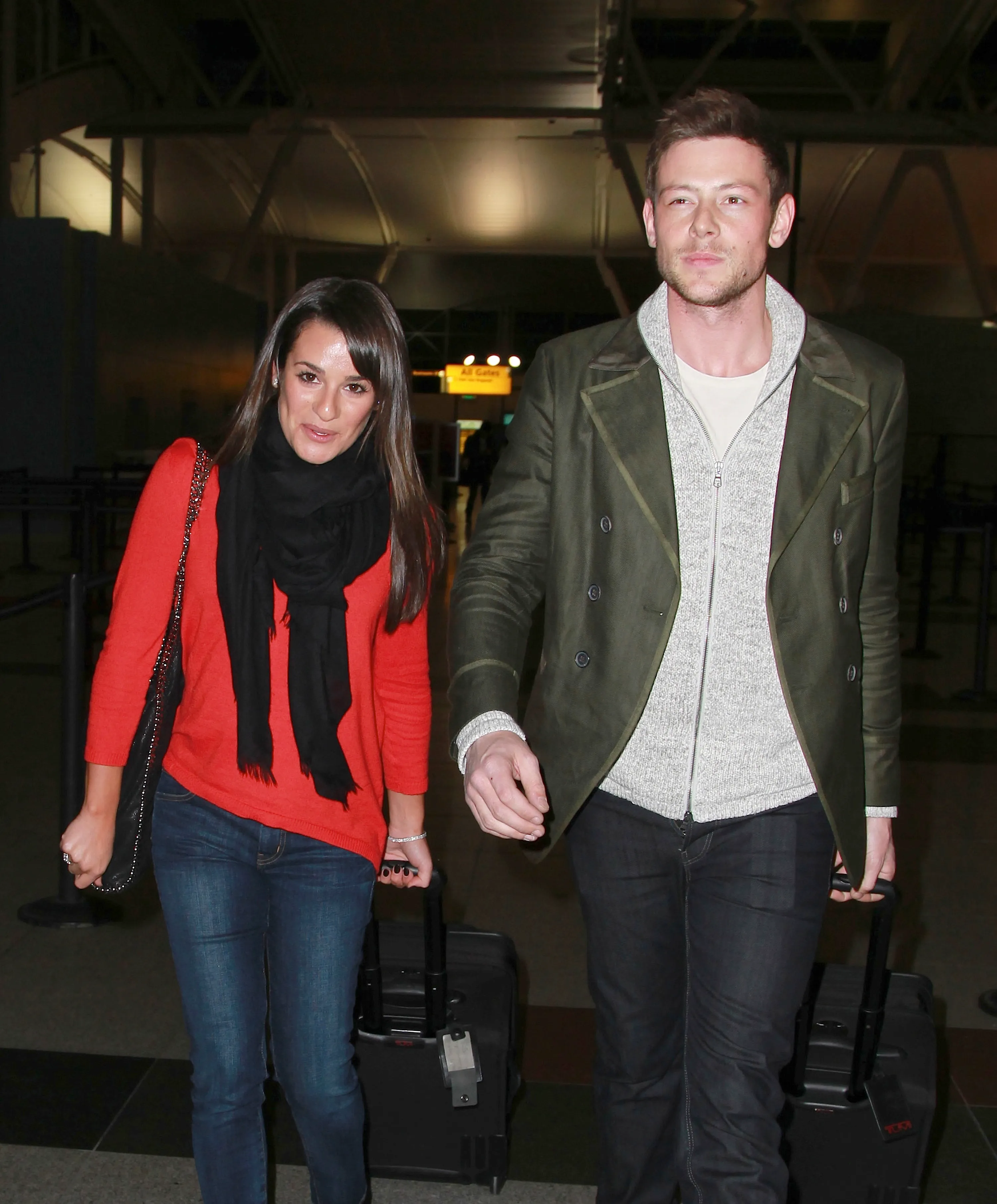 Lea Michele and Cory Monteith walk through JFK Airport, pulling luggage.