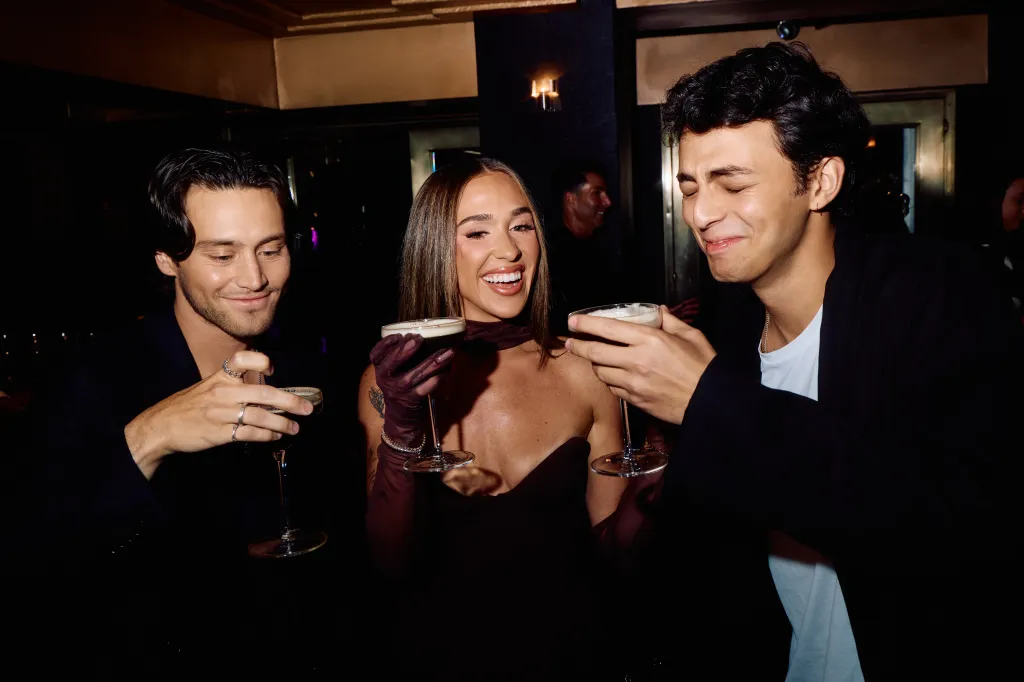 Liam Obergfoll, Ariana Biermann, and Shai Fruchter hold cocktail glasses and smile together.