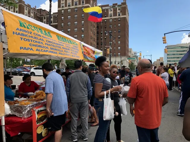 A street food vendor with a yellow sign listing Hispanic dishes is busy serving customers at an outdoor fair.
