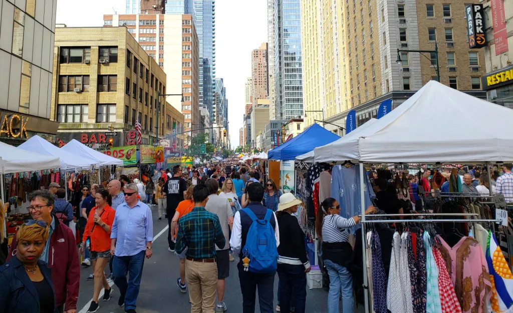 A busy street fair in New York City with vendors, tents, and shoppers lining the avenue.