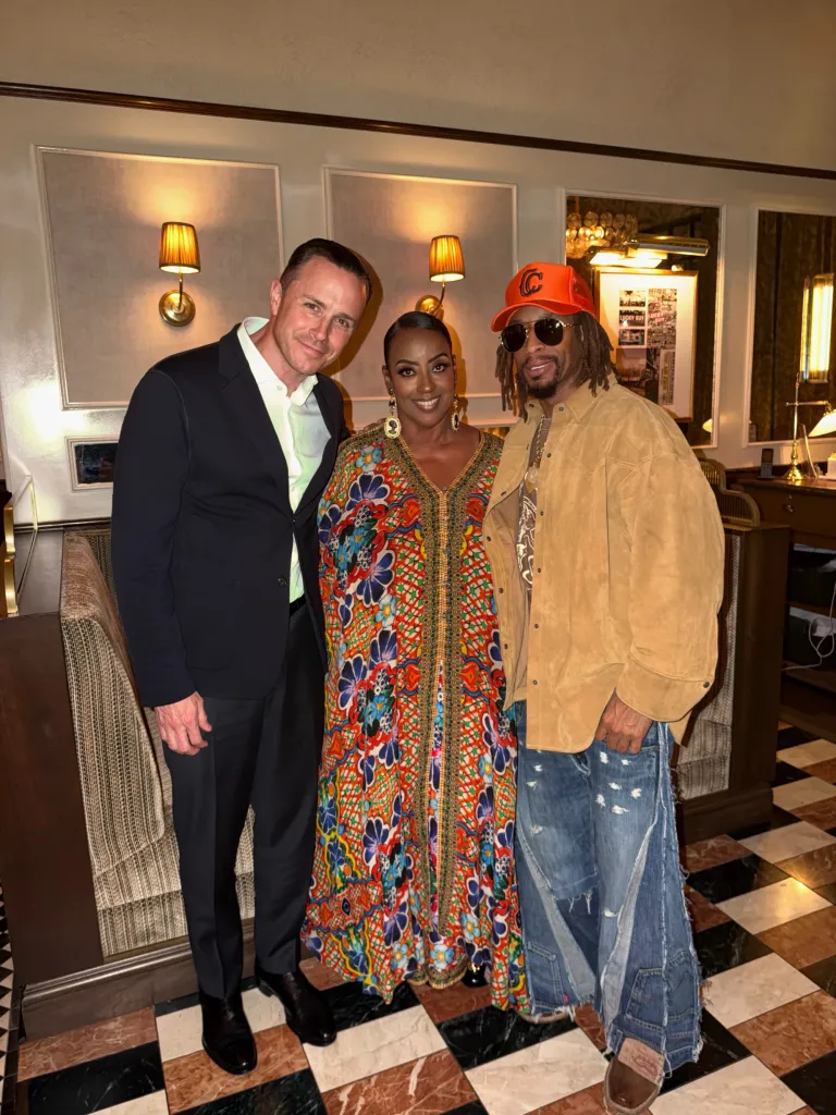 Lil Jon, wearing an orange hat and sunglasses, poses with two other people inside a restaurant.