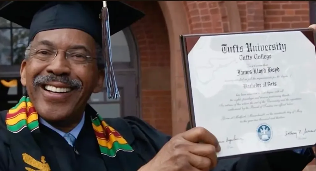 Jim Boyd smiling in graduation cap and gown while holding his Tufts University diploma.