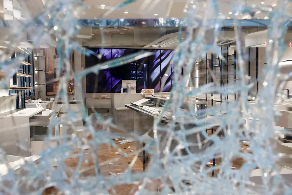 A Christian Dior store looted and vandalized in Paris, viewed through a shattered window.