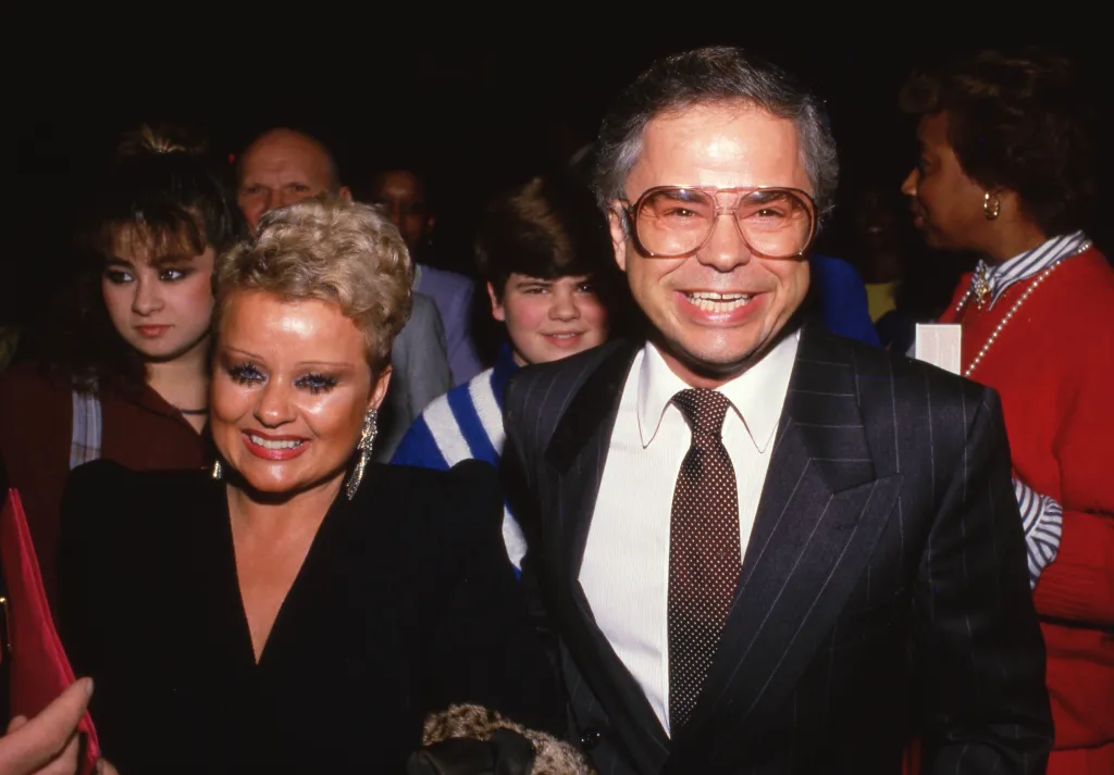 Jim Bakker and his wife Tammy Faye smiling together in a crowd.