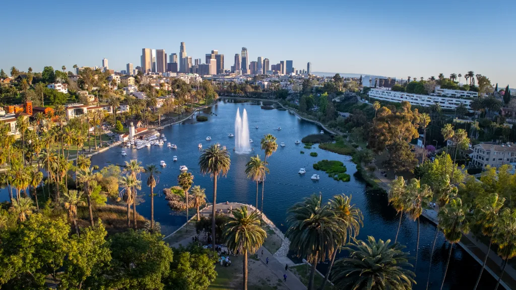 Aerial view of Echo Park Lake in Los Angeles, California, with palm trees and a fountain, featuring the downtown skyline in the background.