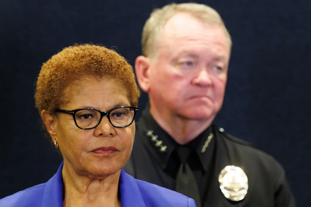 Los Angeles Mayor Karen Bass stands at a press conference at LAPD HQ, with an officer standing behind her.