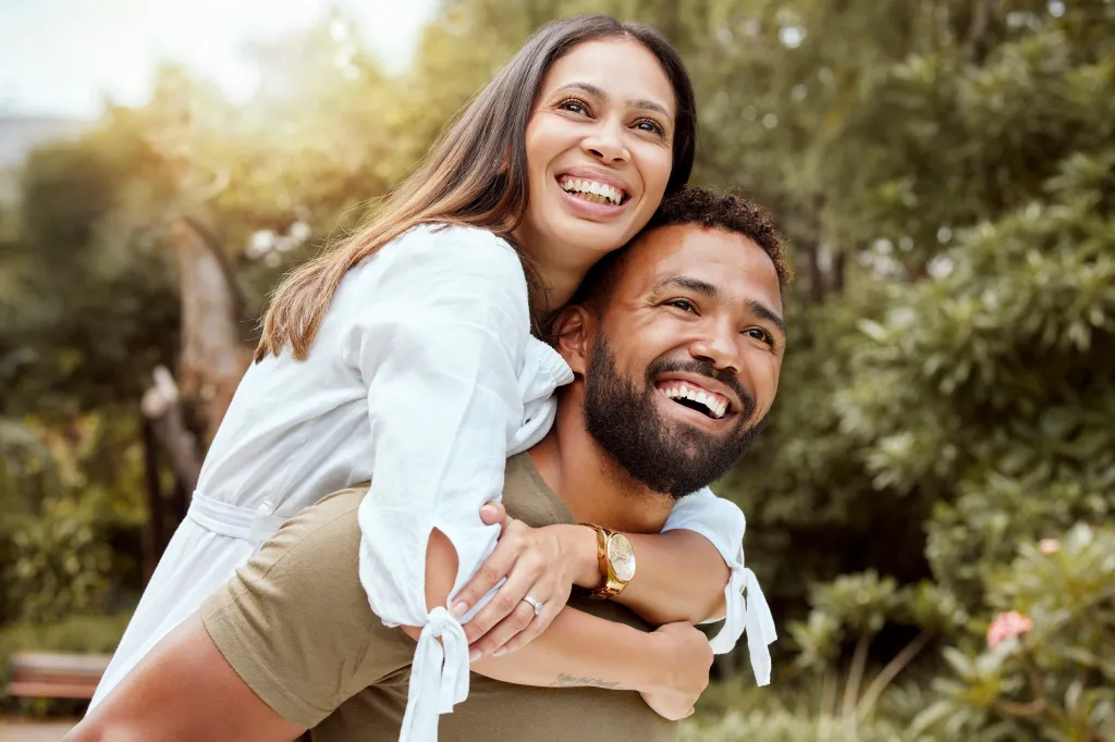 A man giving a woman a piggyback ride in a sunny park.