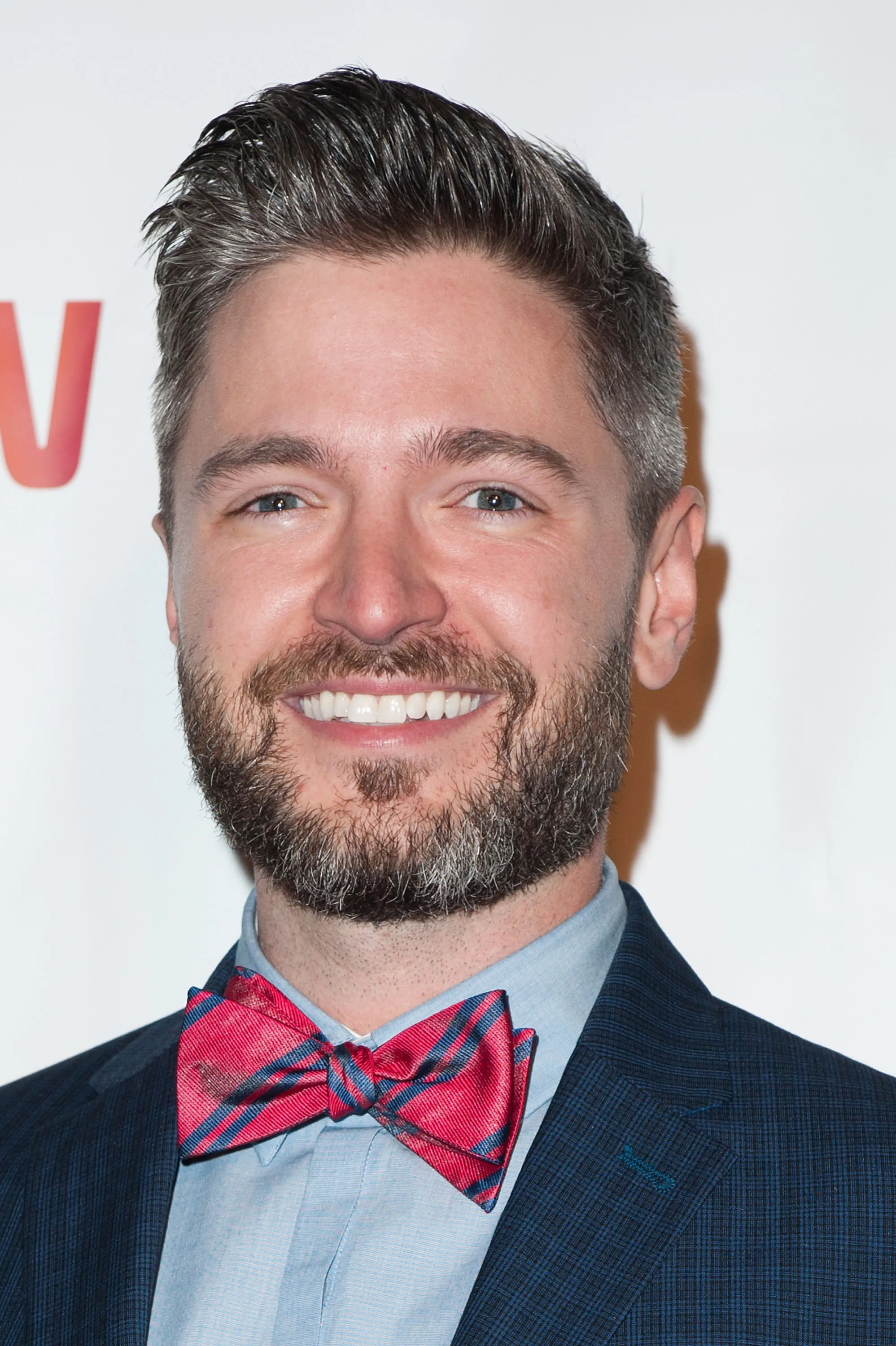 Lucian Piane smiling while wearing a suit jacket and red plaid bow tie.