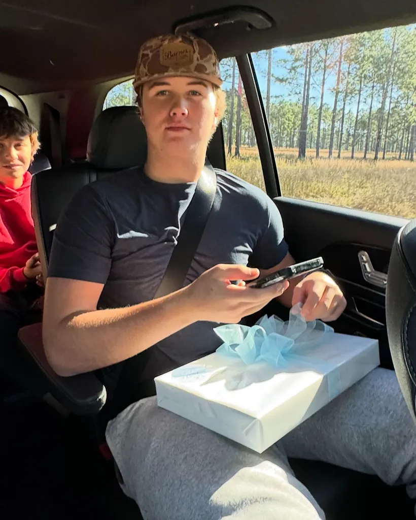 Thomas Boyer Bryan sitting in a car holding a wrapped gift and a phone.