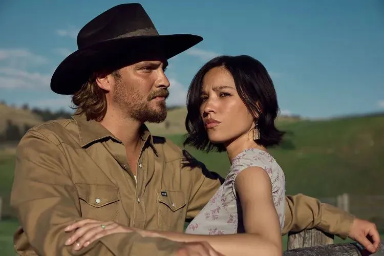 Luke Grimes and Kelsey Asbille outdoors in a rural setting.