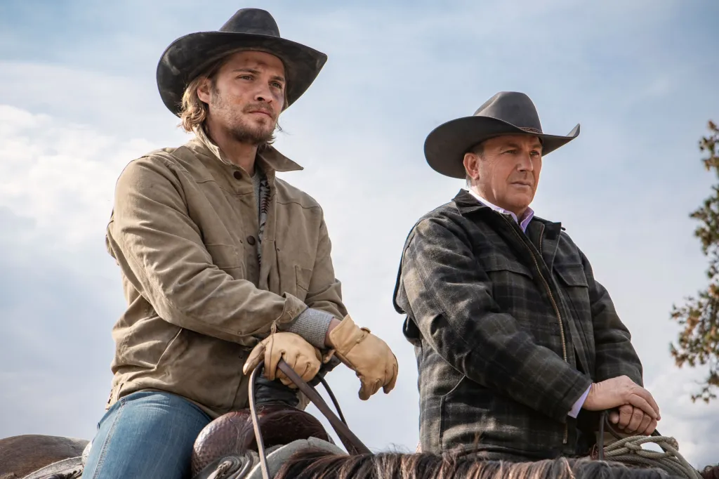 Luke Grimes and Kevin Costner wearing cowboy hats and jackets while on horseback in Yellowstone.