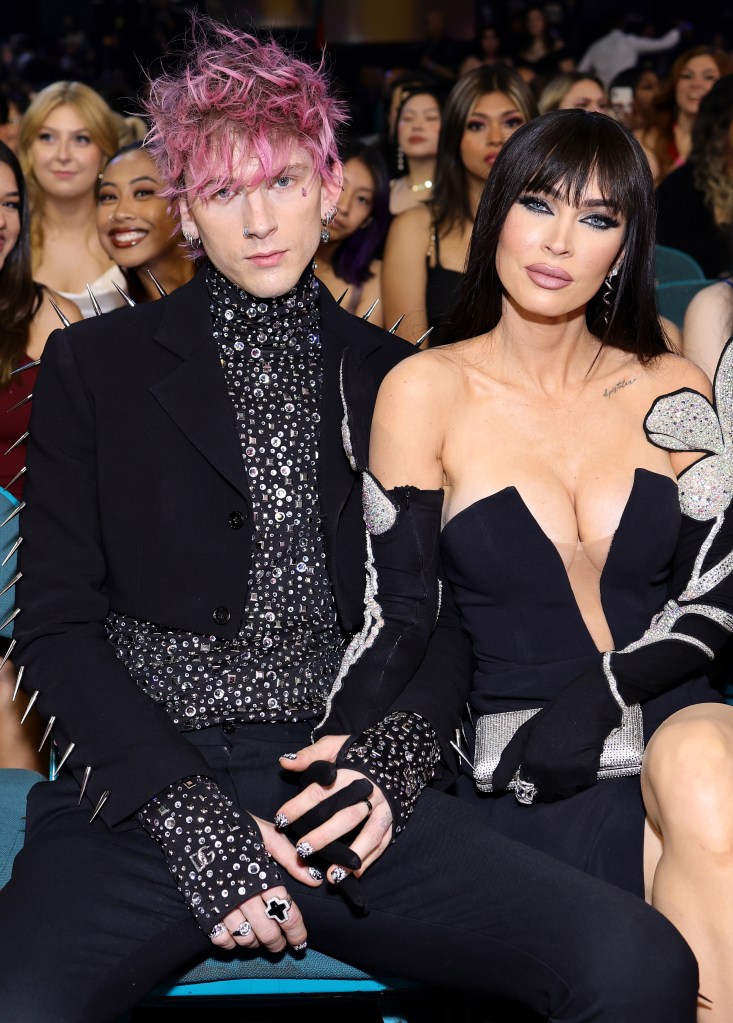 Machine Gun Kelly and Megan Fox seated together, holding hands.