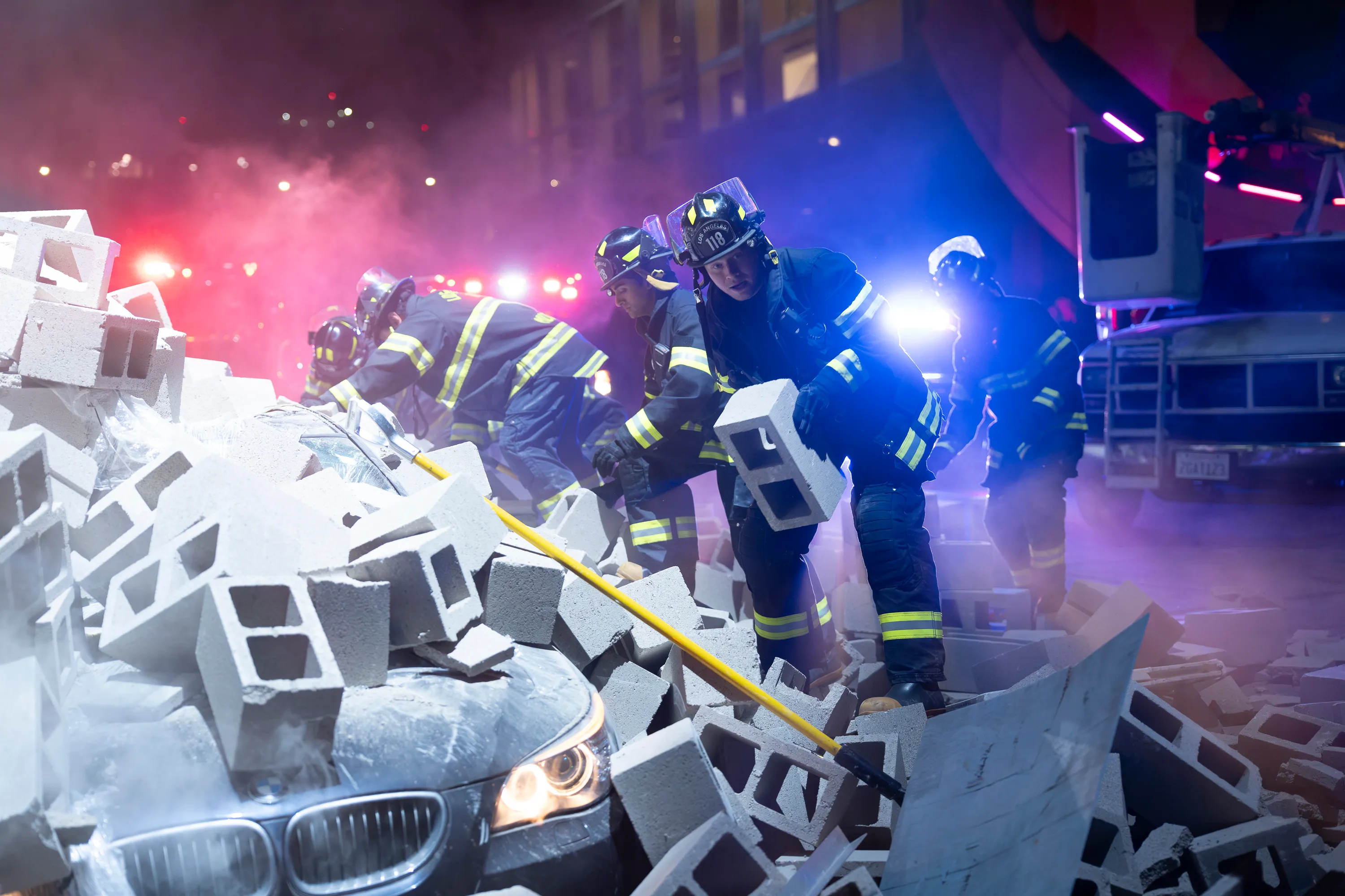 Firefighters clear away concrete blocks from a crushed car at a night rescue scene.