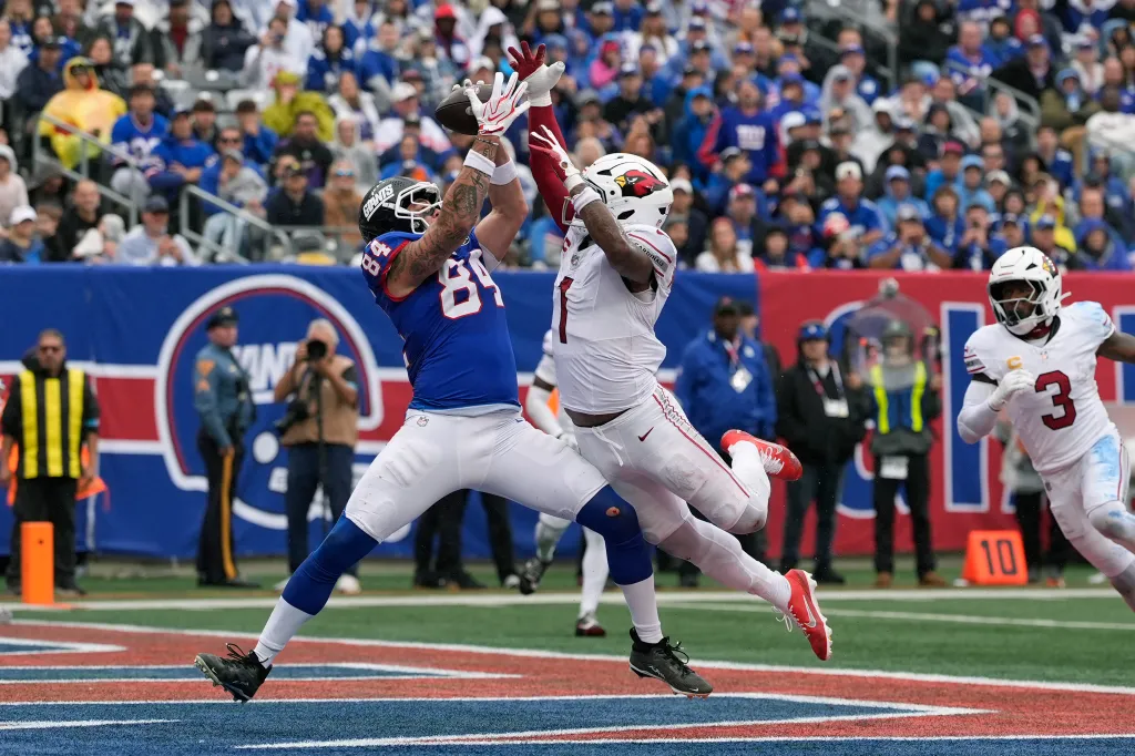 New York Giants tight end Theo Johnson makes a touchdown catch against Arizona Cardinals linebacker Mack Wilson Sr. as Cardinals safety Budda Baker looks on.
