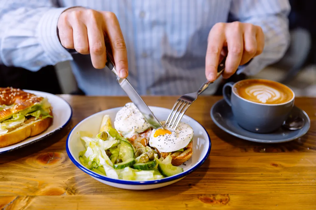 A man eating a breakfast of poached eggs, fresh salad and coffee.