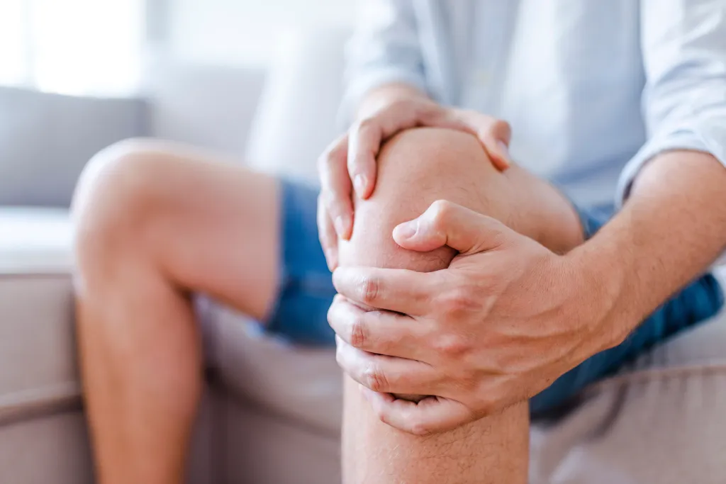 A man holding his painful knee while sitting on a sofa.