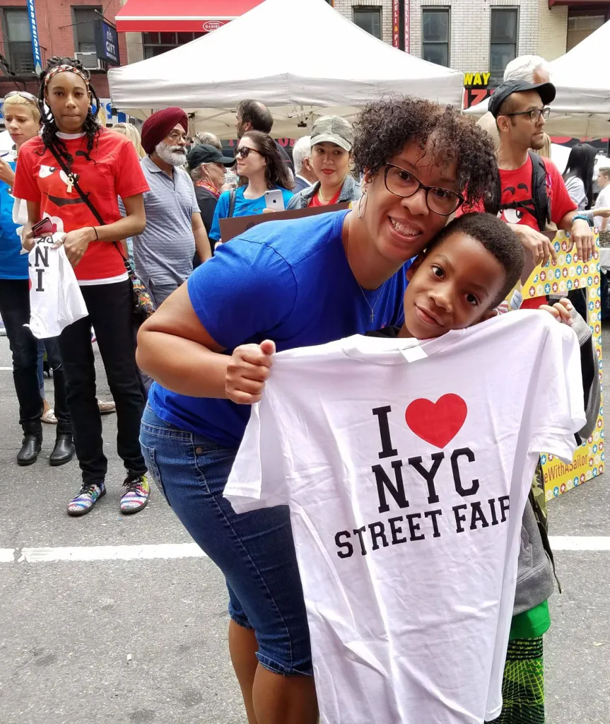 A woman and a young boy smiling and holding up a white T-shirt that reads