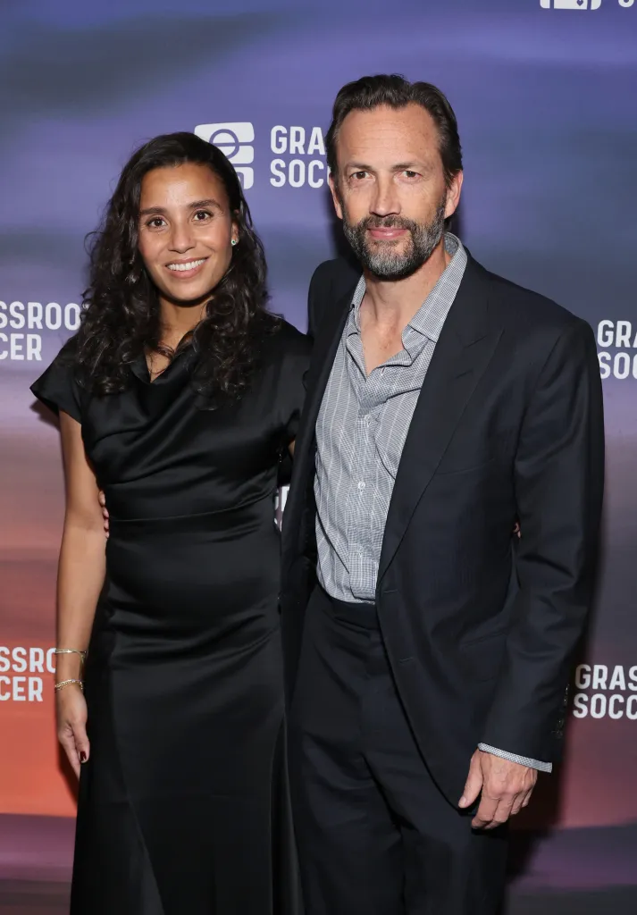 Marilee Fiebig and Andrew Shue pose together on a purple-lit step-and-repeat backdrop for the Grassroot Soccer World AIDS Day Gala.