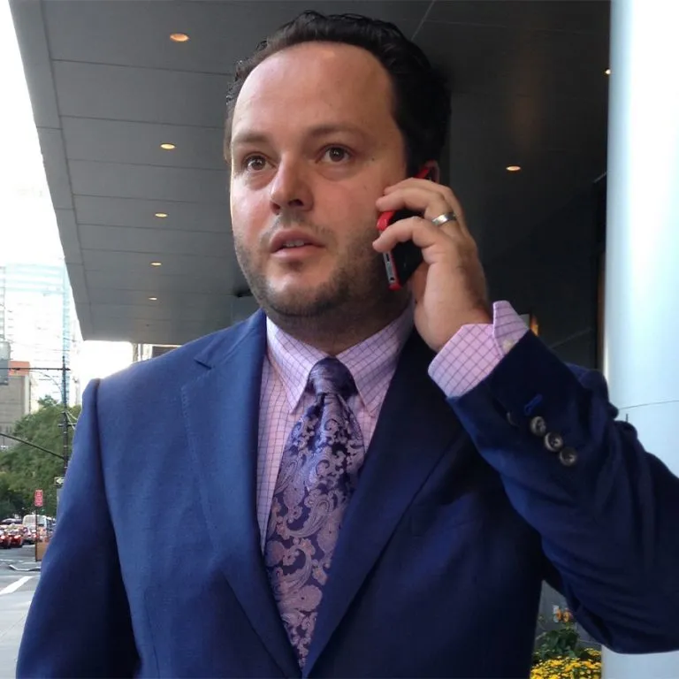 Mario Govic talking on a phone outdoors, wearing a blue suit and a patterned tie.