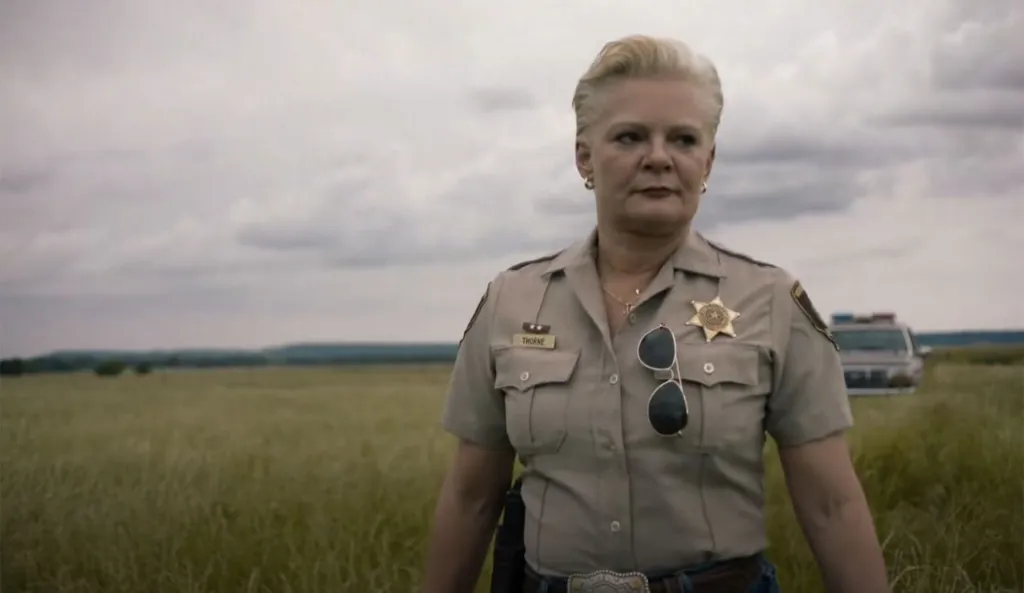 Martha Plimpton as Martha Thorne in a police uniform in a field.