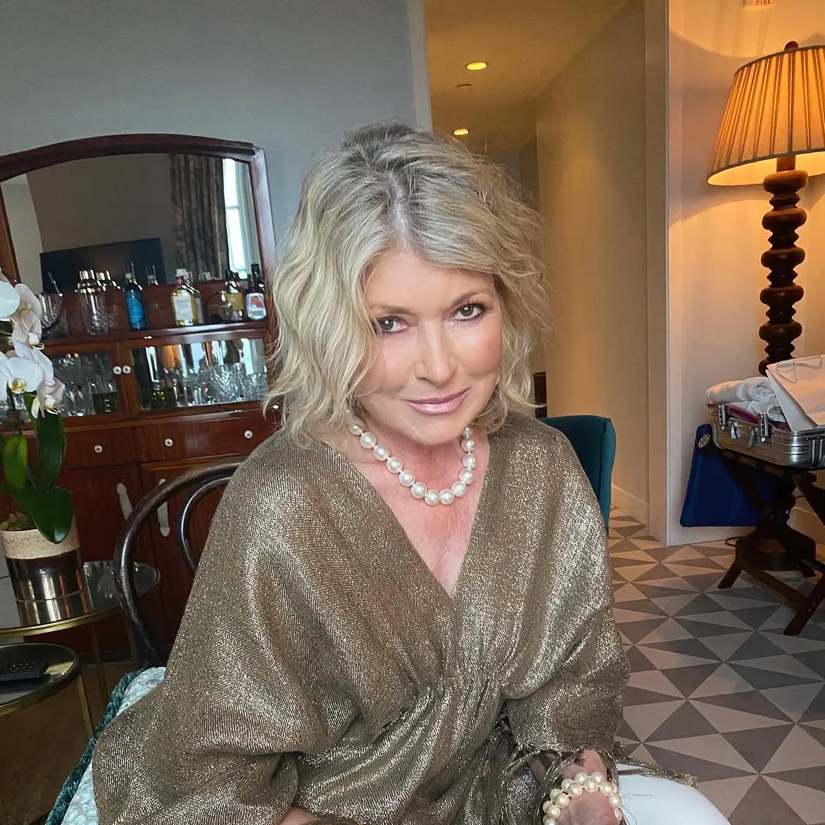 Martha Stewart wearing a gold top and a pearl necklace indoors.