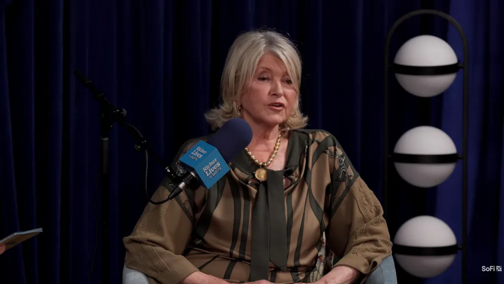 Martha Stewart speaks into a microphone while sitting in front of a blue curtain.