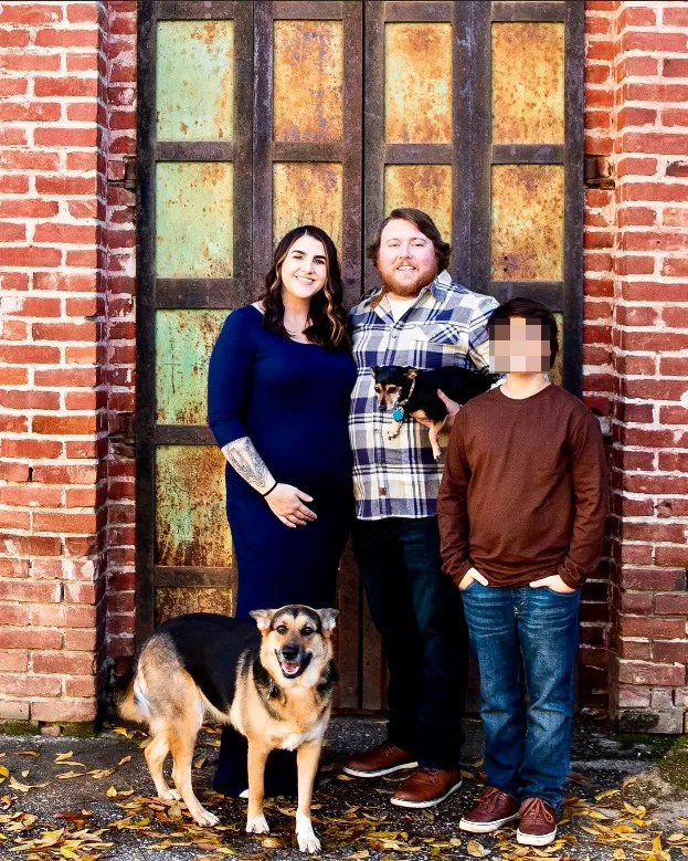 Martina poses with her three sons in front of a brick wall and a rustic door.