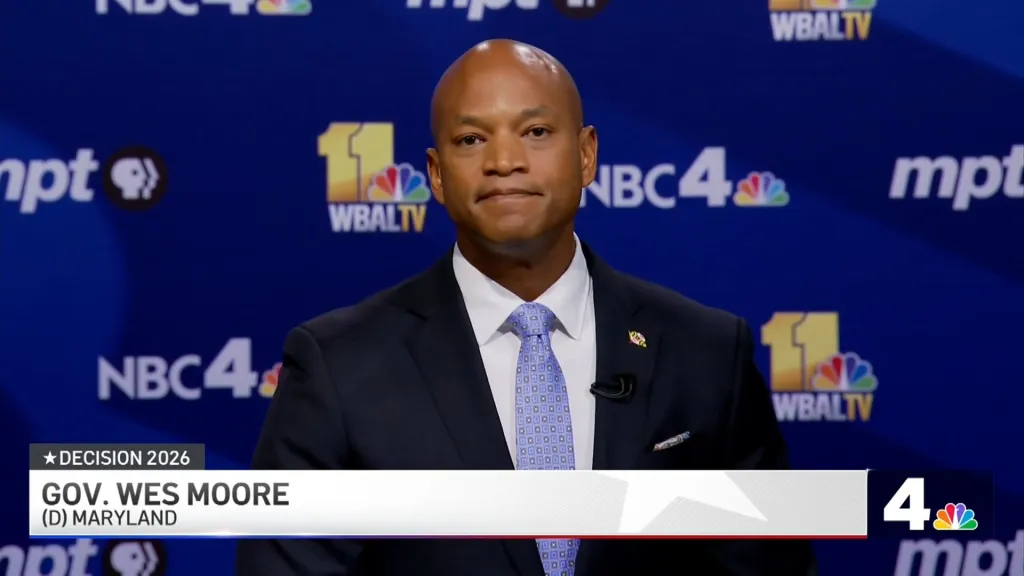 Maryland Gov. Wes Moore standing before a debate backdrop with news channel logos.