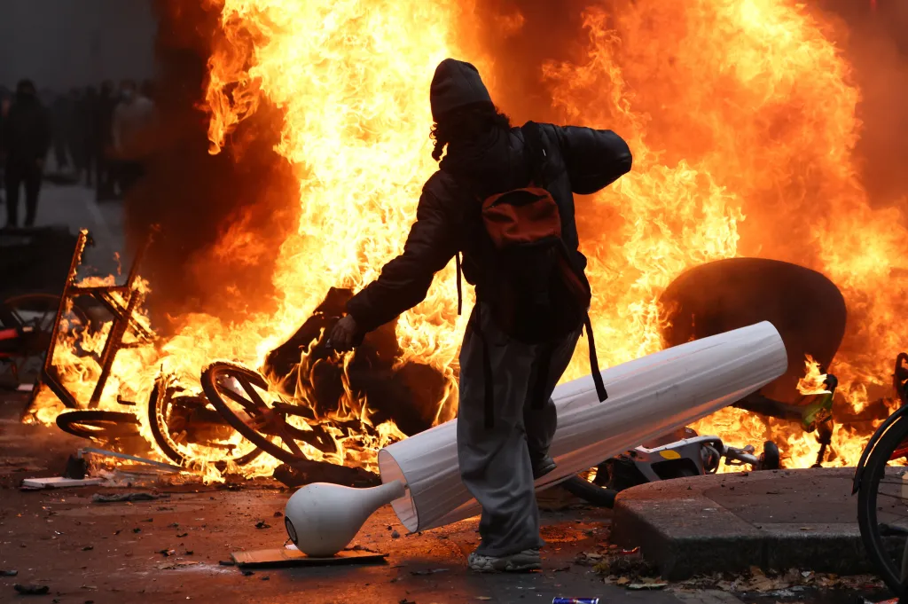 Masked protestors throwing objects form vandalized stores into a burning pile